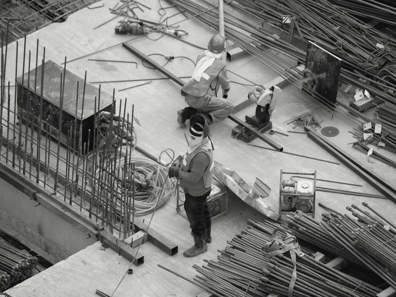 Vista superior de una losa en obra con varilla, herramienta y dos trabajadores con equipo de protección.